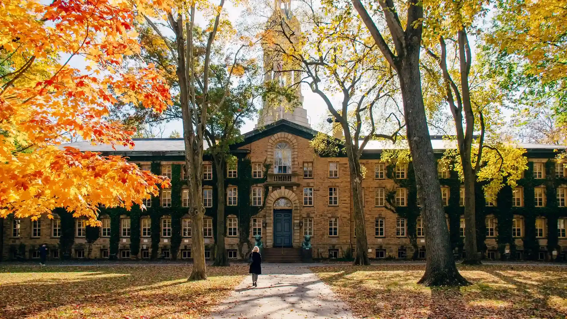 Autumn trees next to large pathway with women walking up to a grand US college